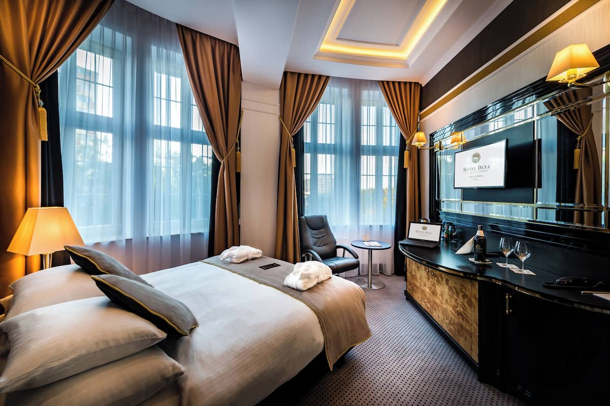 A hotel room with a large bed, a sitting area with a chair and a small table, a minibar, and a large mirror.