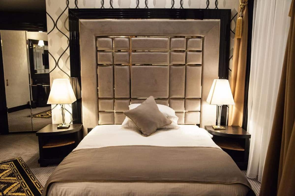 A hotel room with a large bed, two bedside lamps, a headboard with a grid pattern, and a patterned rug.