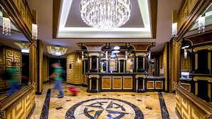 A grand lobby with a large chandelier, a reception desk, and a distinctive circular floor design.