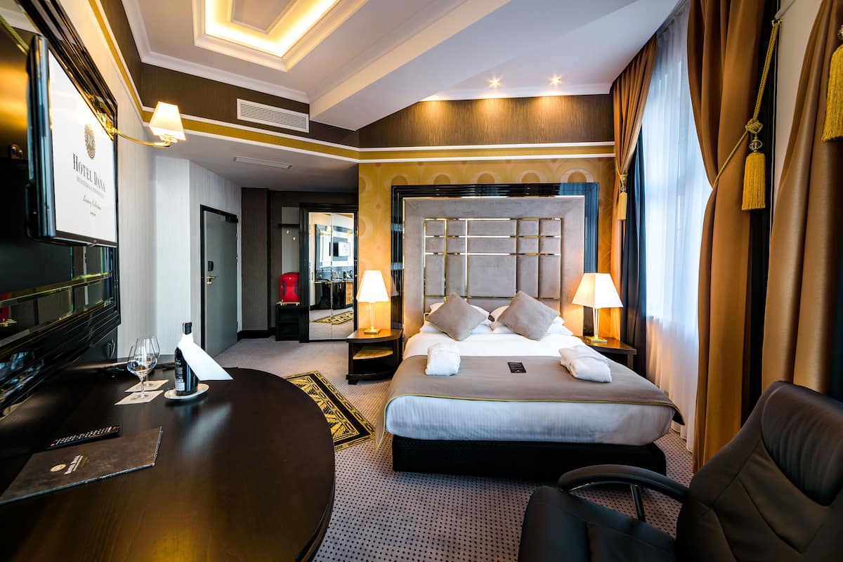 A hotel room with a large bed, a desk with a computer, a chair, and a television.