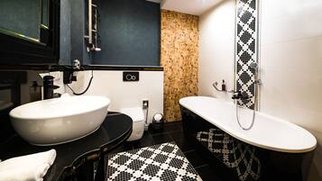 A modern bathroom with a large white sink, a black toilet, and a freestanding bathtub with a black and white patterned tile backsplash.