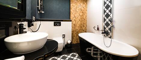 Un baño moderno con un lavamanos grande blanco, un inodoro negro y una bañera independiente con un salpicadero de azulejos con estampado blanco y negro.