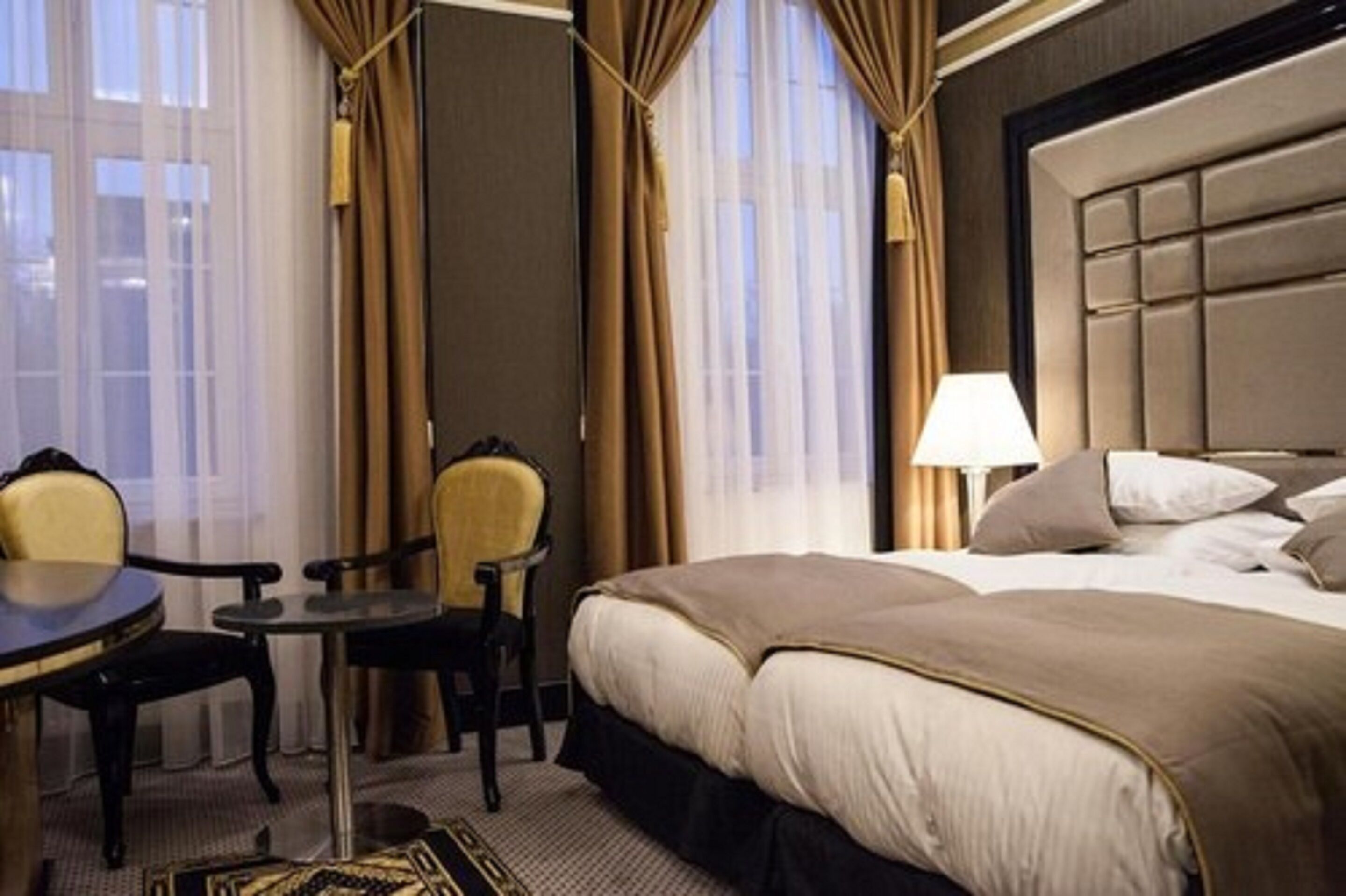Une chambre d’hôtel avec un grand lit, une petite table, deux chaises et une lampe.