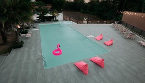En pool med en rosa uppblåsbar flamingofigur, omgiven av solstolar och parasoller.