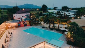 Zona de piscina con un mural, asientos al aire libre y montañas al fondo.