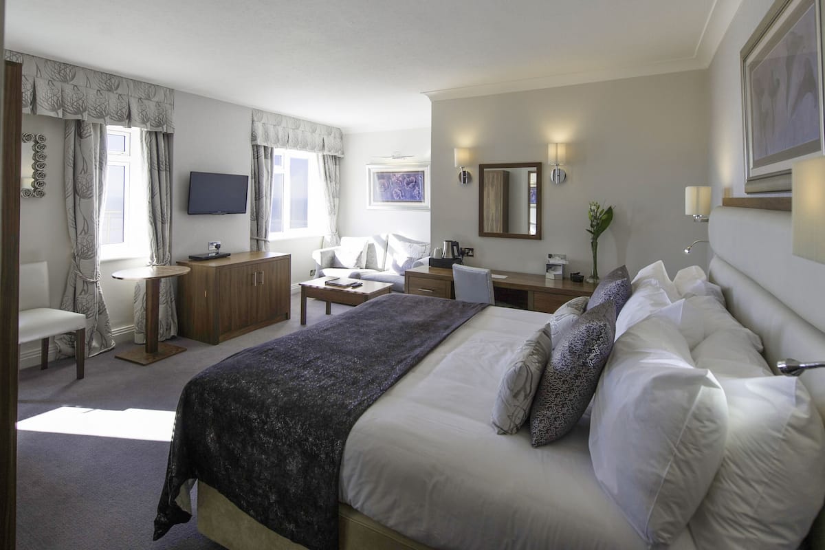 Ein Hotelzimmer mit einem großen Bett, einem Schreibtisch, einem Stuhl, einem Fernseher und einem Fenster mit Vorhängen.