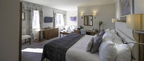 A hotel room with a large bed, a desk, a chair, a TV, and a window with curtains.