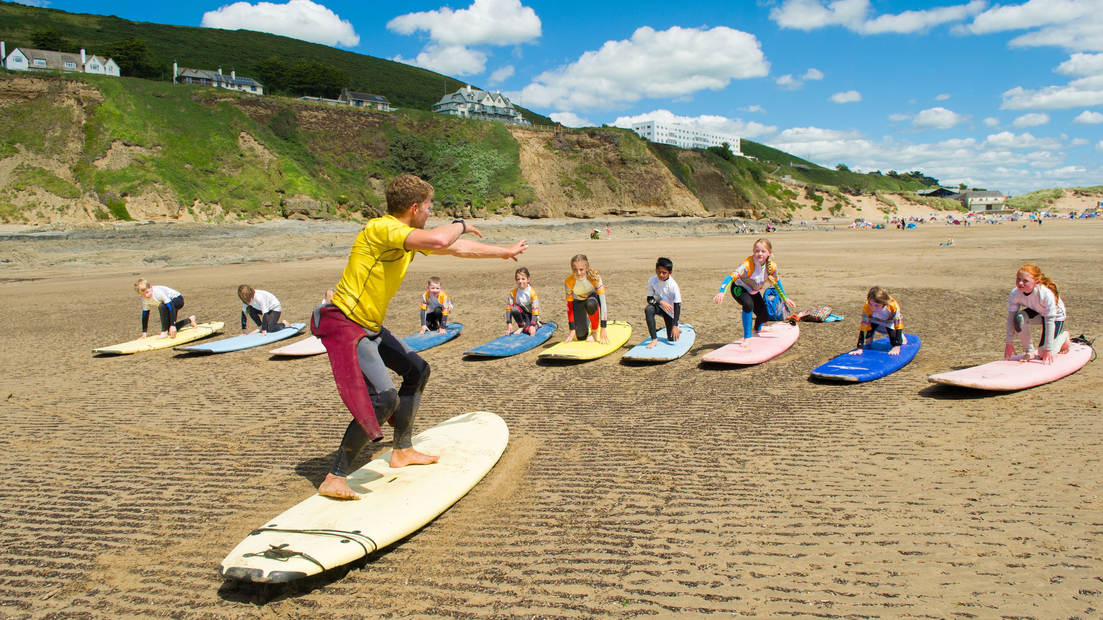 A beach with people on surfboards, a sandy beach, and a hill with buildings in the background.