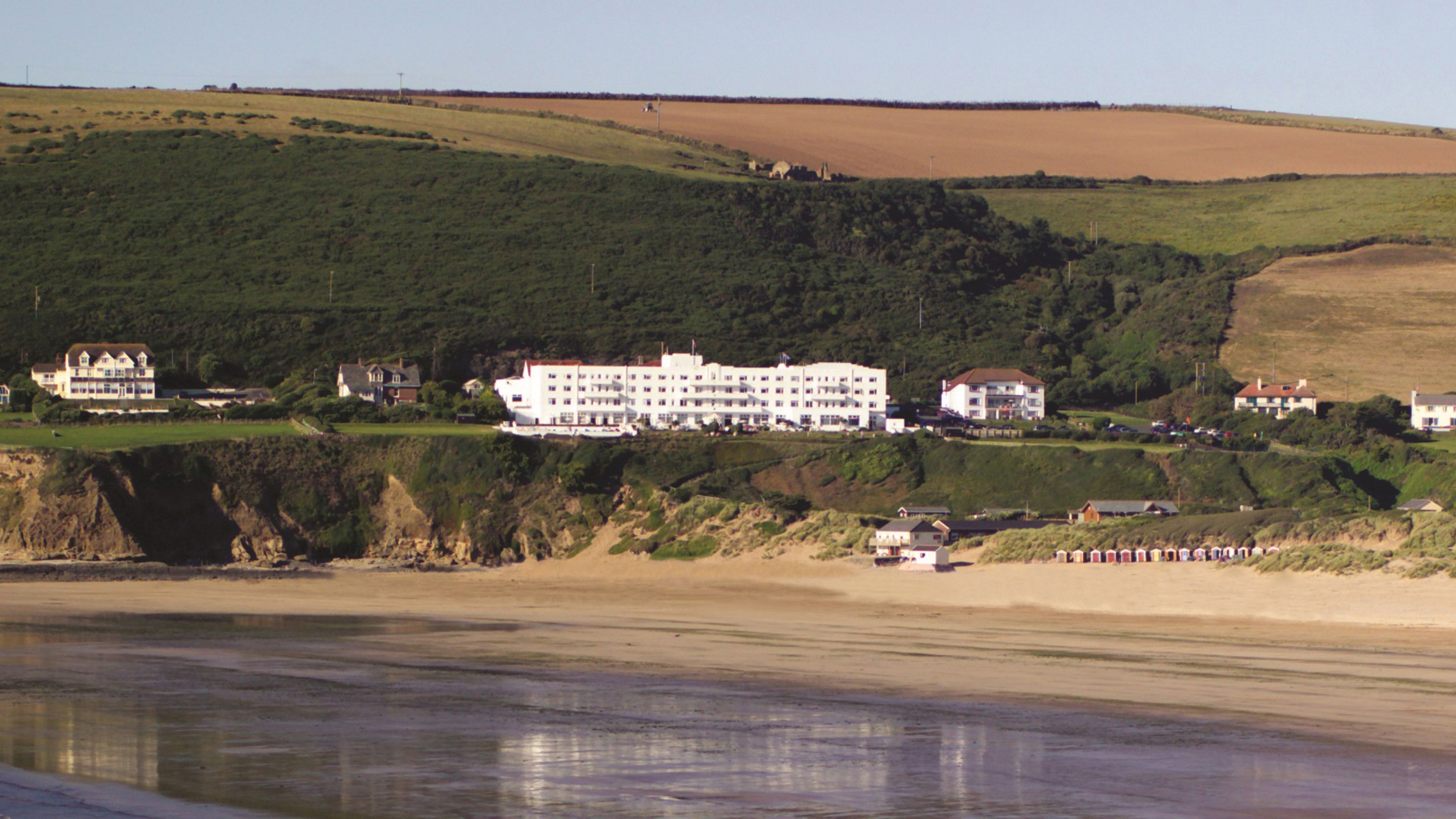 A coastal hotel with multiple buildings, a beach, and a cliffside.