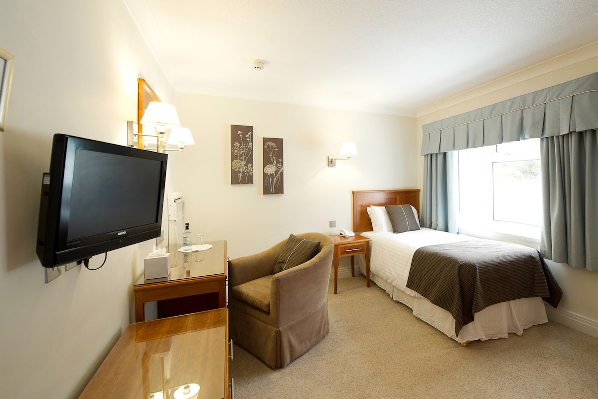Ein Hotelzimmer mit Bett, Fernseher, Schreibtisch, Stuhl und einem Fenster mit Vorhängen.