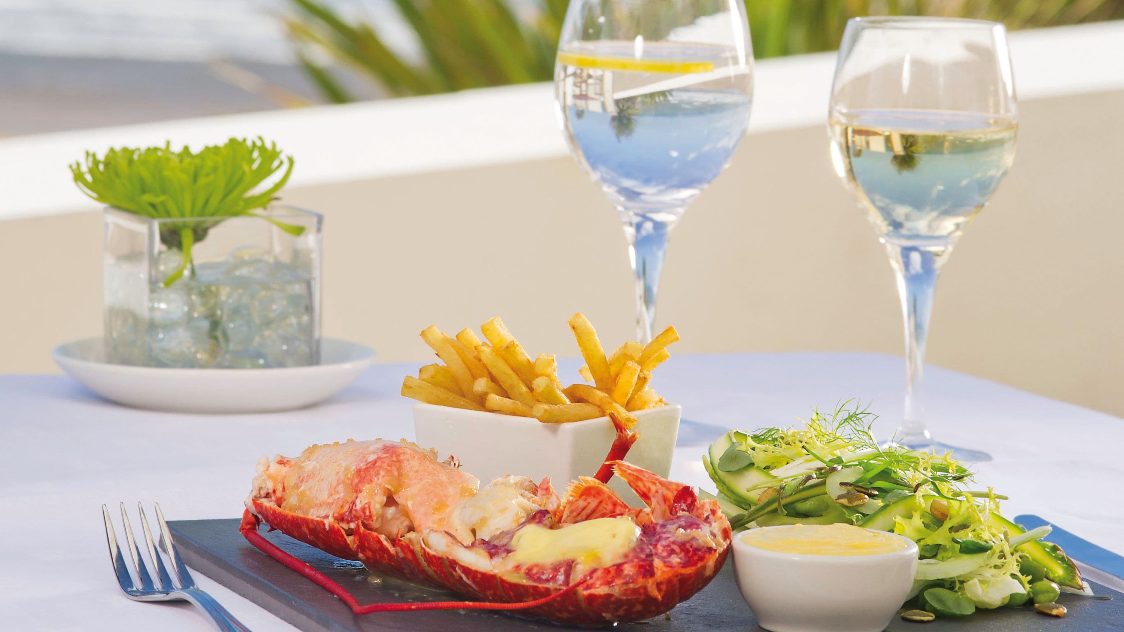 Une table avec un homard, des frites, une salade et deux verres d’eau.