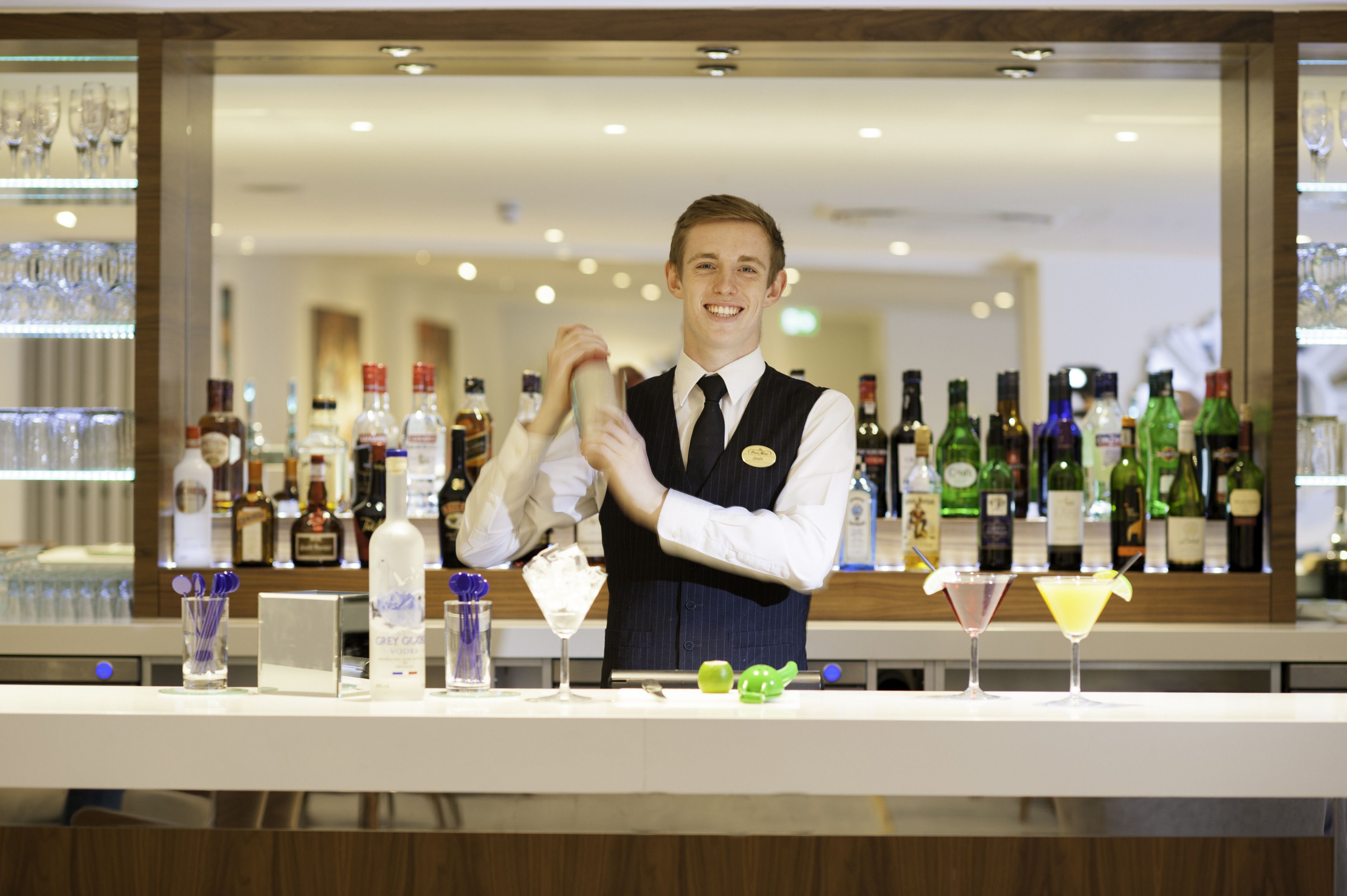 A bar area with a bartender preparing drinks, a variety of bottles, and glasses on the counter.