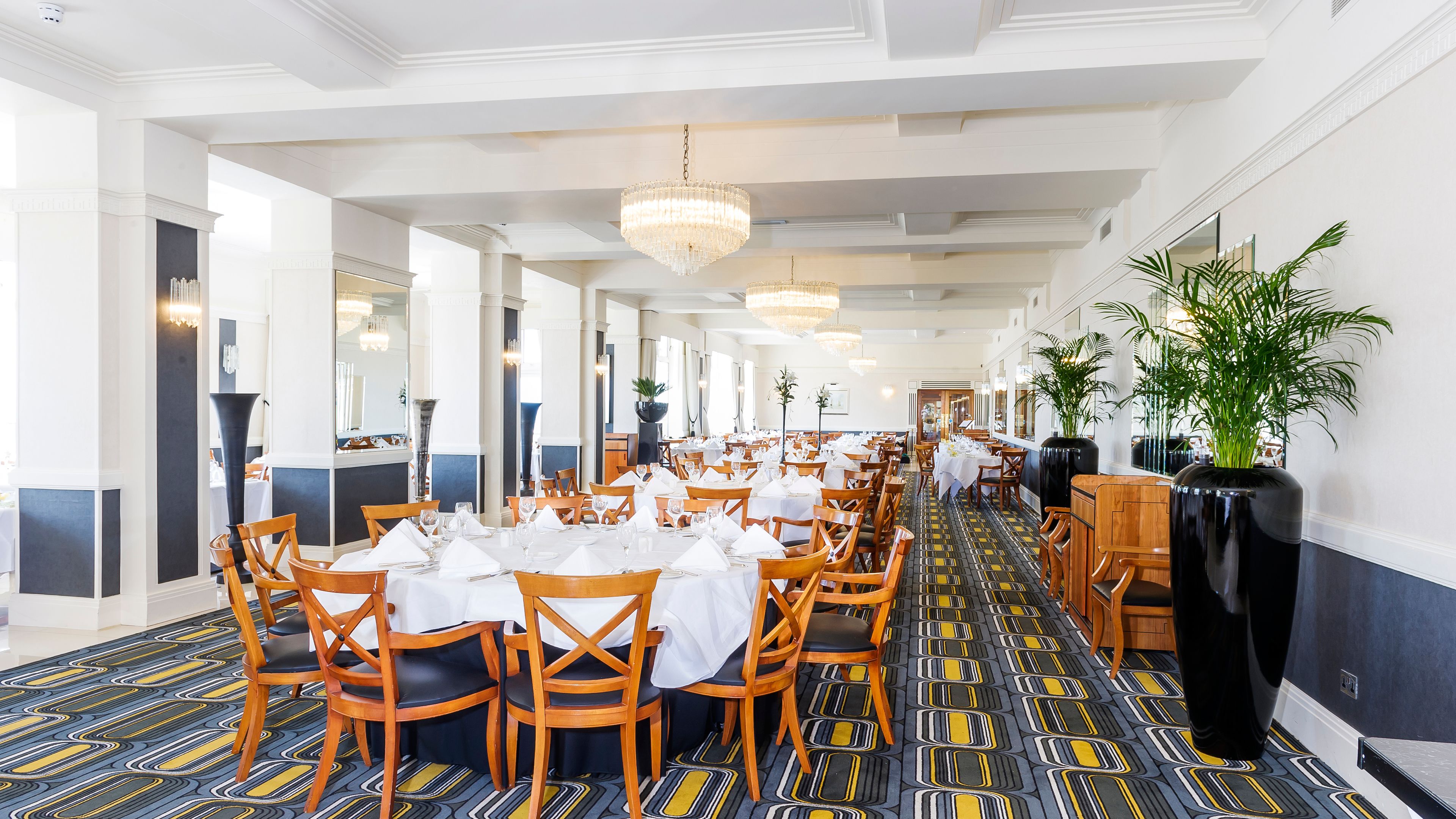 Une salle à manger d’hôtel spacieuse, avec de longues tables, des chaises en bois et un sol à motifs.