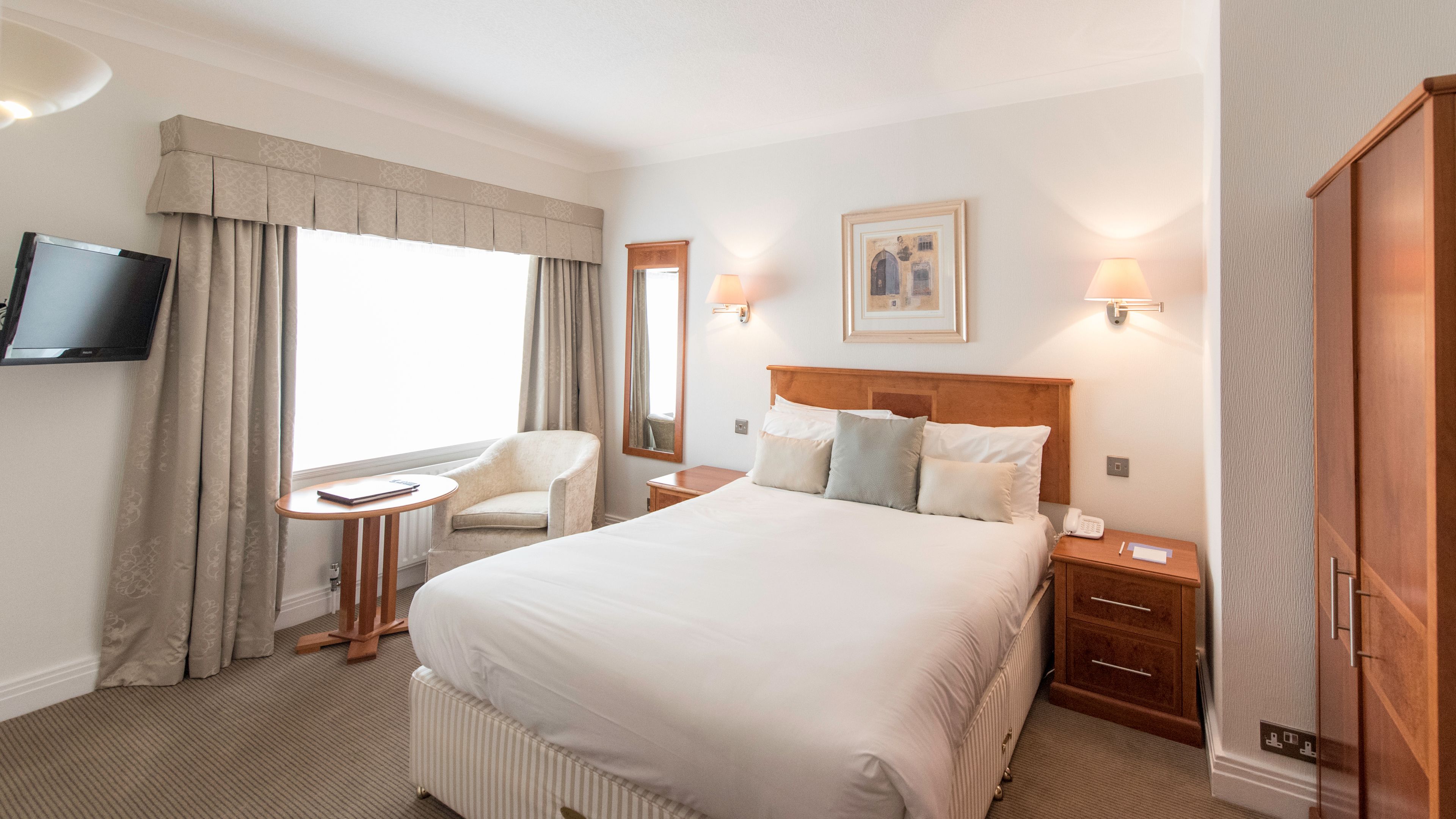 Een hotelkamer met een groot bed, een bureau, een stoel, een televisie en een schilderij aan de muur.