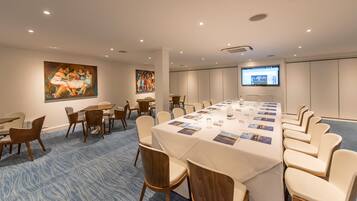 Un salón de conferencias con una larga mesa, sillas y una pantalla para proyector.