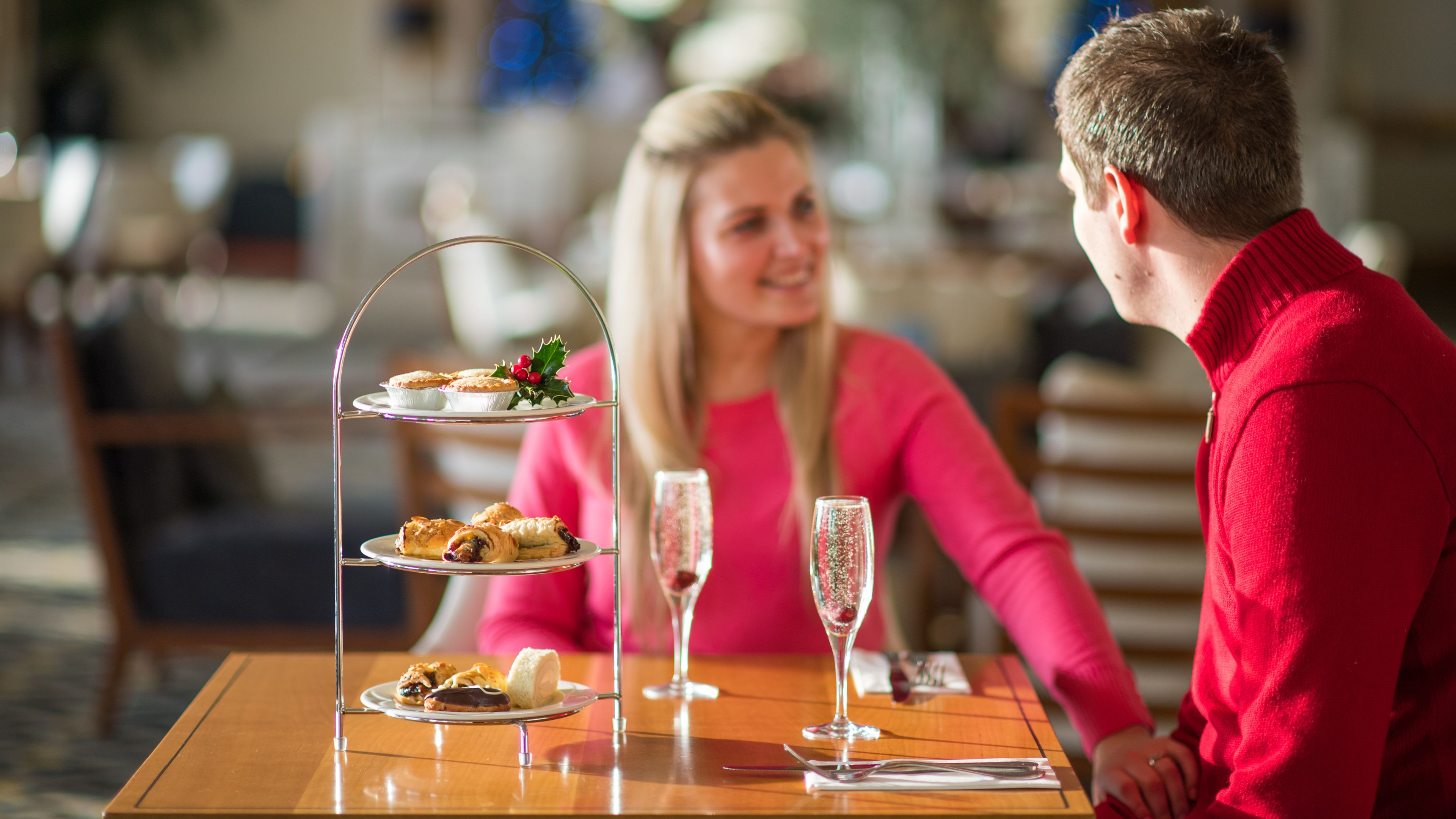 A dining table with a three-tiered dessert stand, a glass of champagne, and a plate of pastries.
