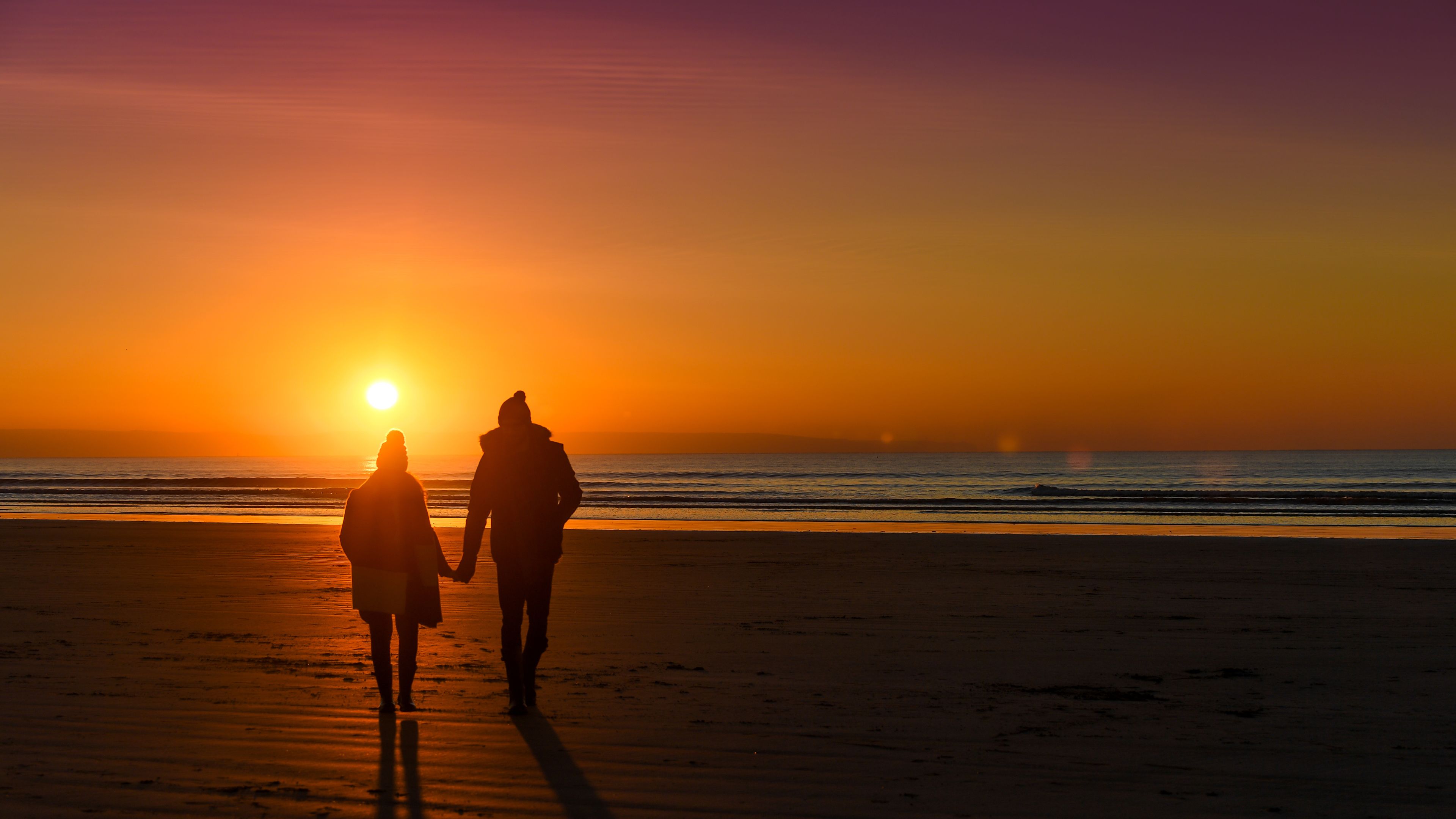 Two people walking on a beach at sunset.