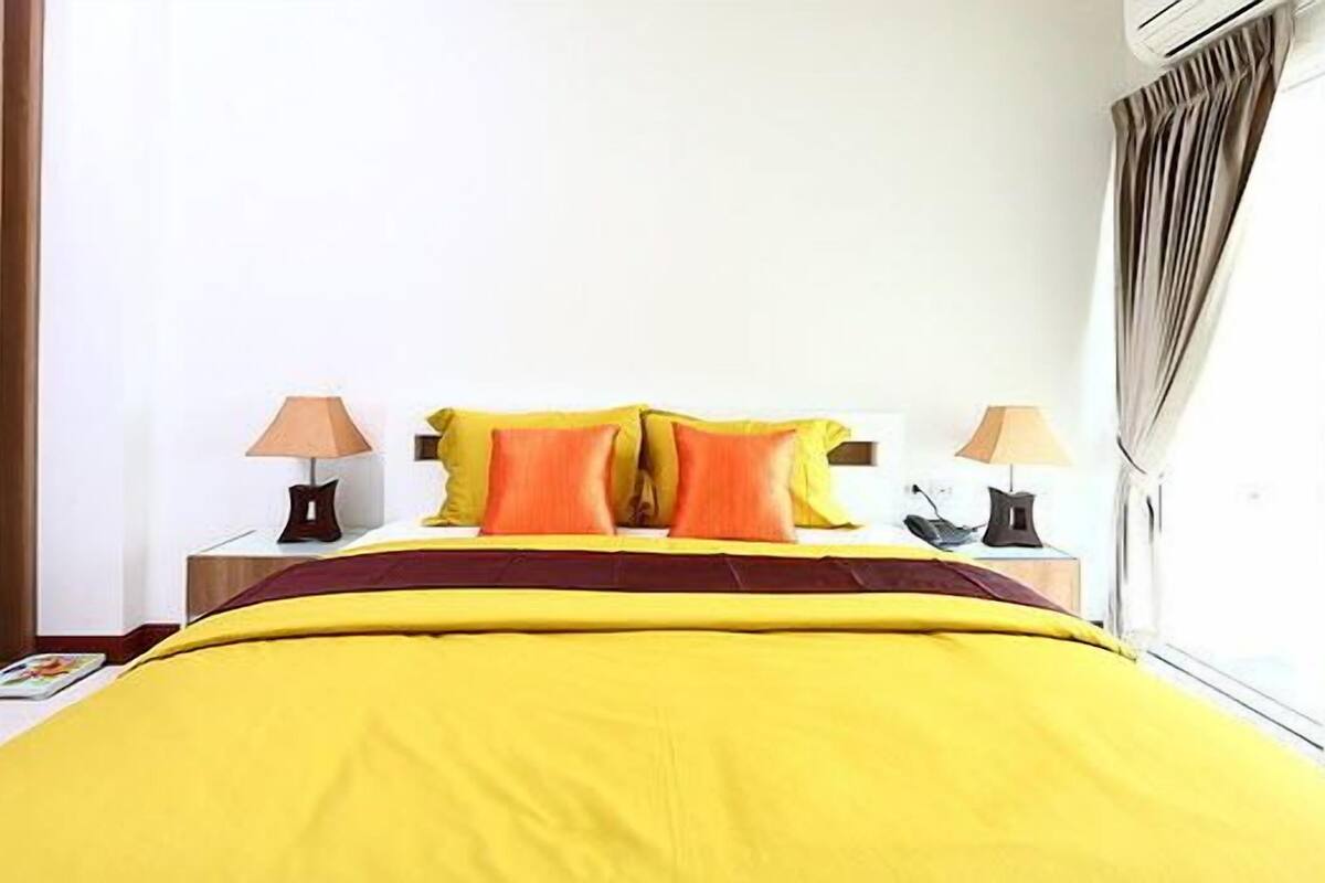 A hotel room with a large bed, two bedside tables, a window with curtains, and a view of the outside.