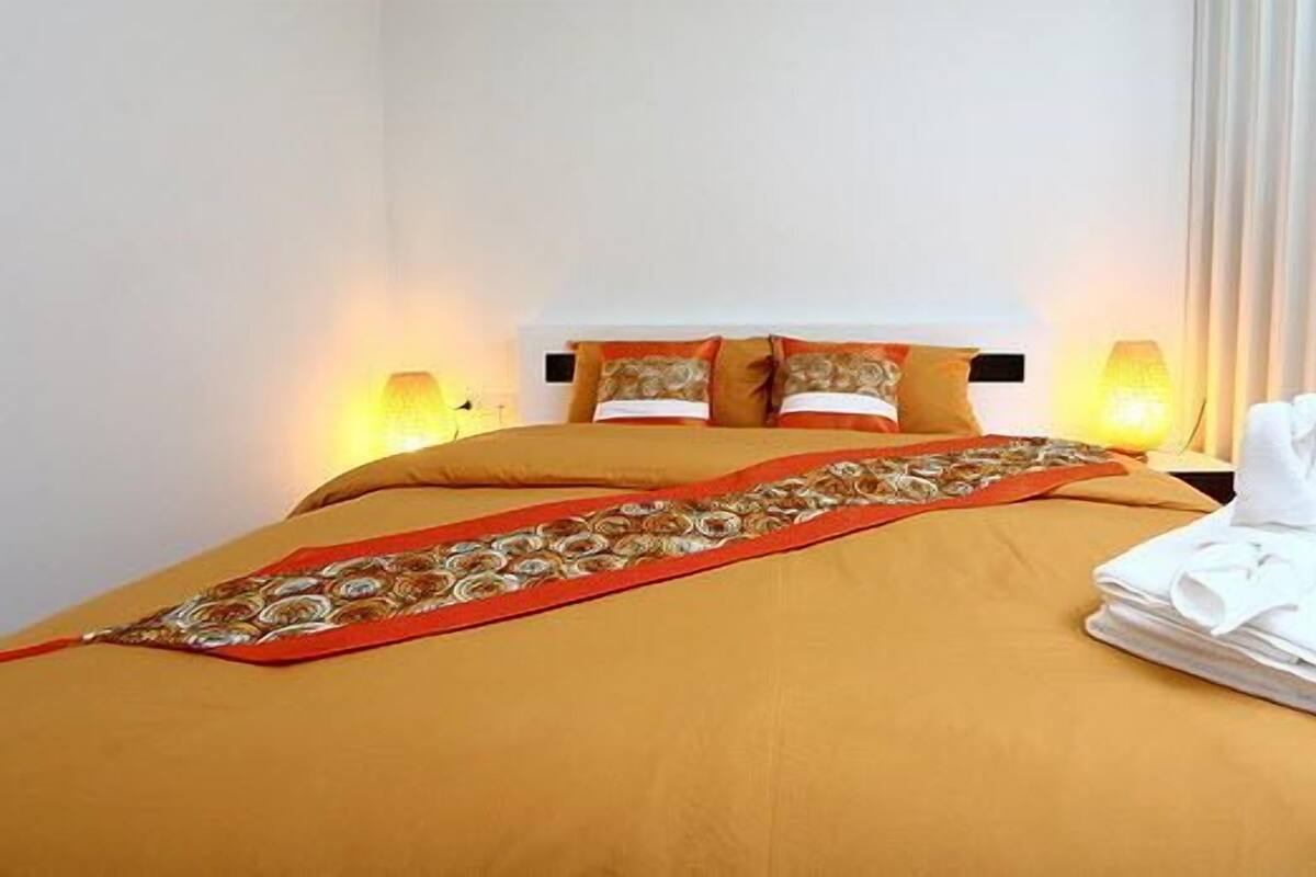 A hotel room with a bed, pillows, a blanket, a folded towel, and a microwave.