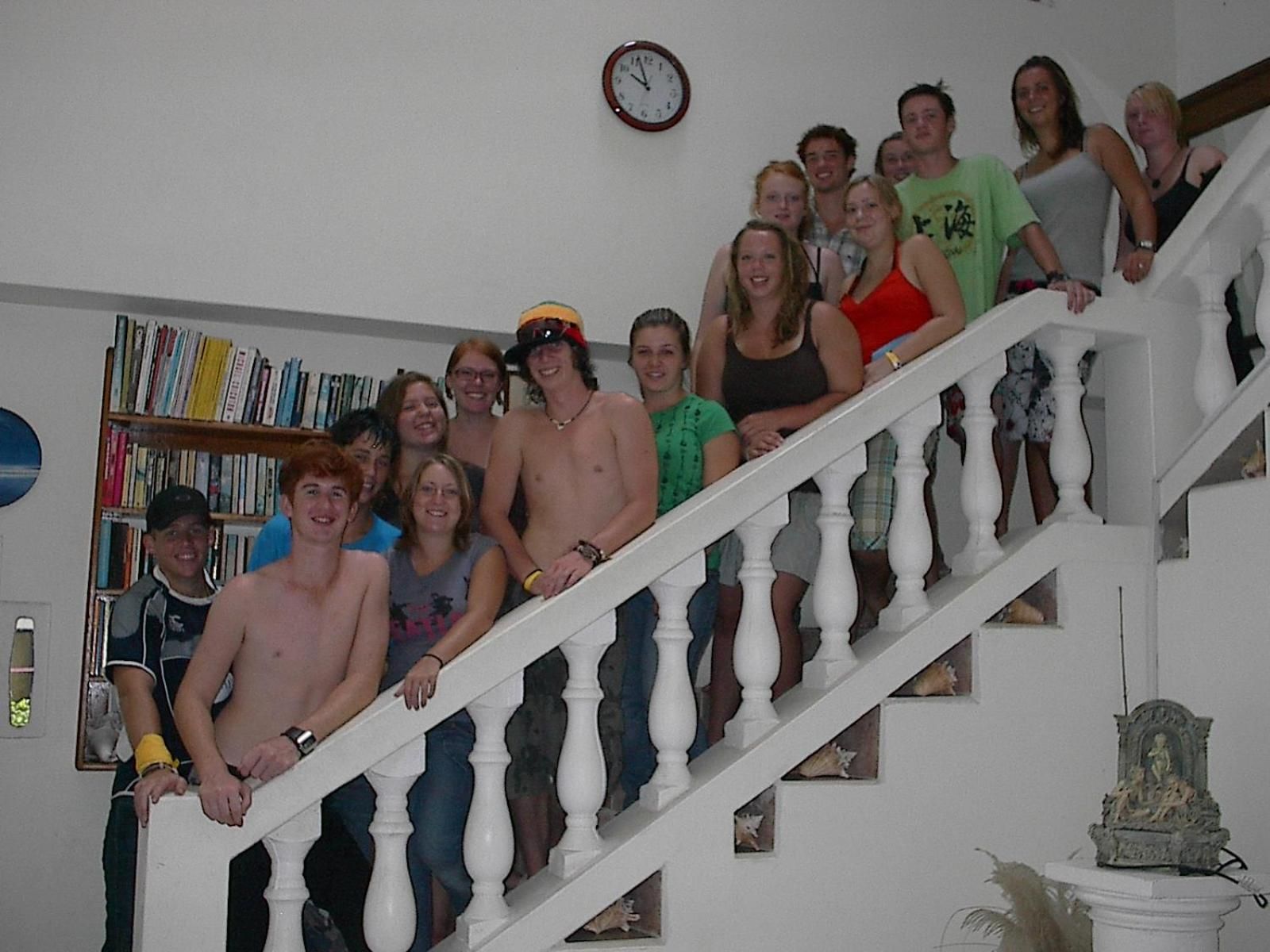 A group of people on a staircase with a bookshelf and a clock in the background.