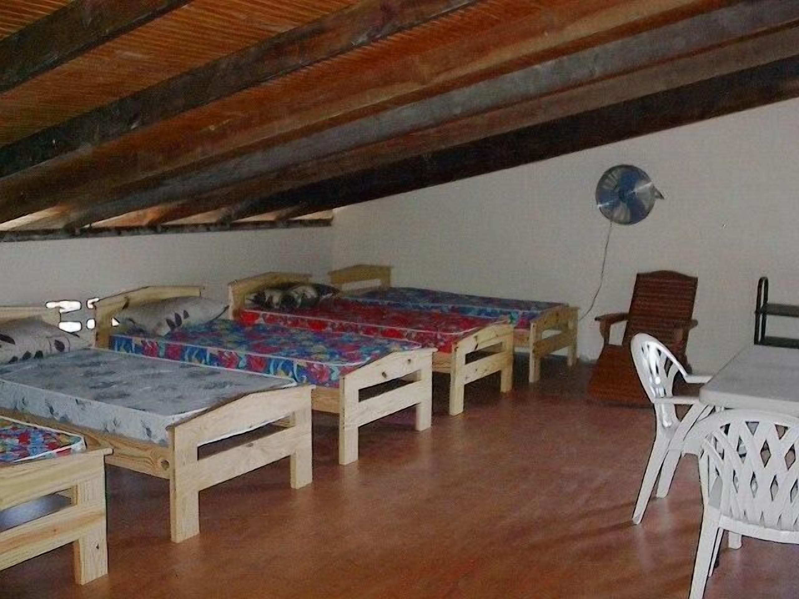 Ein Schlafsaalzimmer mit drei Holzbett, einem weißen Plastikstuhl und einem Tisch.