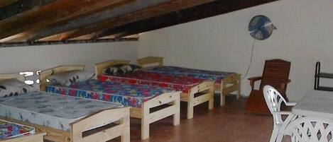 Ein Schlafsaalzimmer mit drei Holzbett, einem weißen Plastikstuhl und einem Tisch.