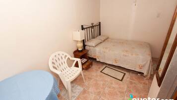 Un dormitorio pequeño con cama, mesita de noche, silla y mesa.