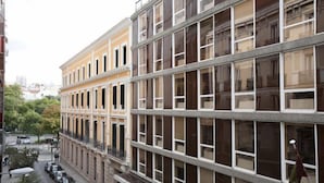 A multi-story building with a row of balconies on the ground floor, a parking area in front, and a clear view of the street. - Hostal Prim (Madrid)
