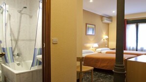 A hotel room with a bathtub, two beds, a chair, and a desk. - Hostal Prim (Madrid)