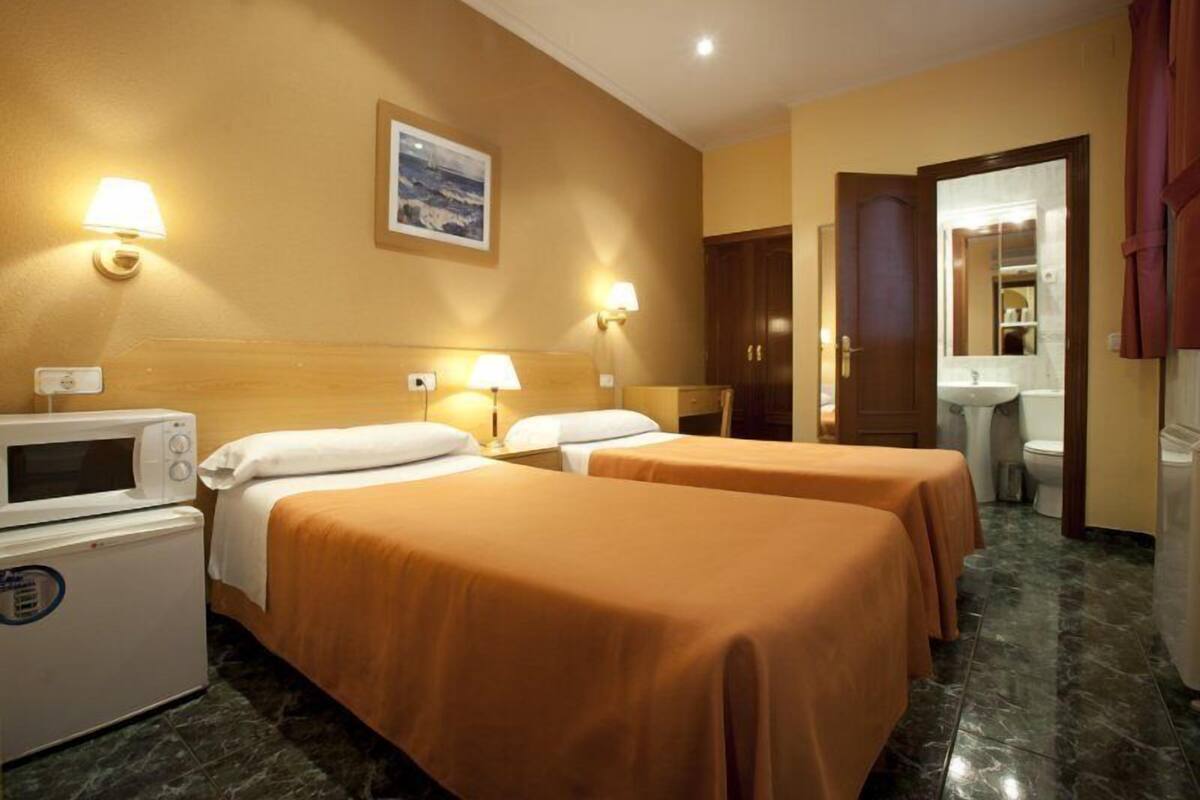 Quarto de hotel com duas camas, micro-ondas, mini-geladeira e banheiro visível por uma porta aberta.