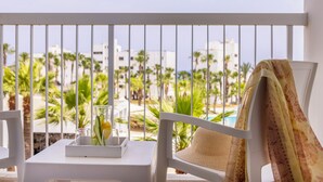 A balcony with a white table, a chair with a woven seat, and a view of palm trees and buildings. - Papantonia Hotel Apartments  (Paralimni)