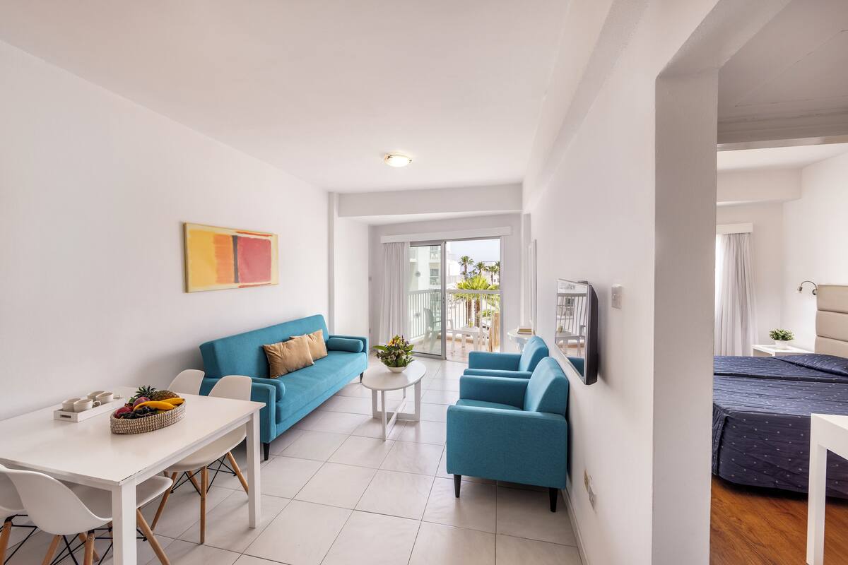 Un salon moderne avec une table blanche, des canapés bleus et un balcon offrant une vue dégagée.