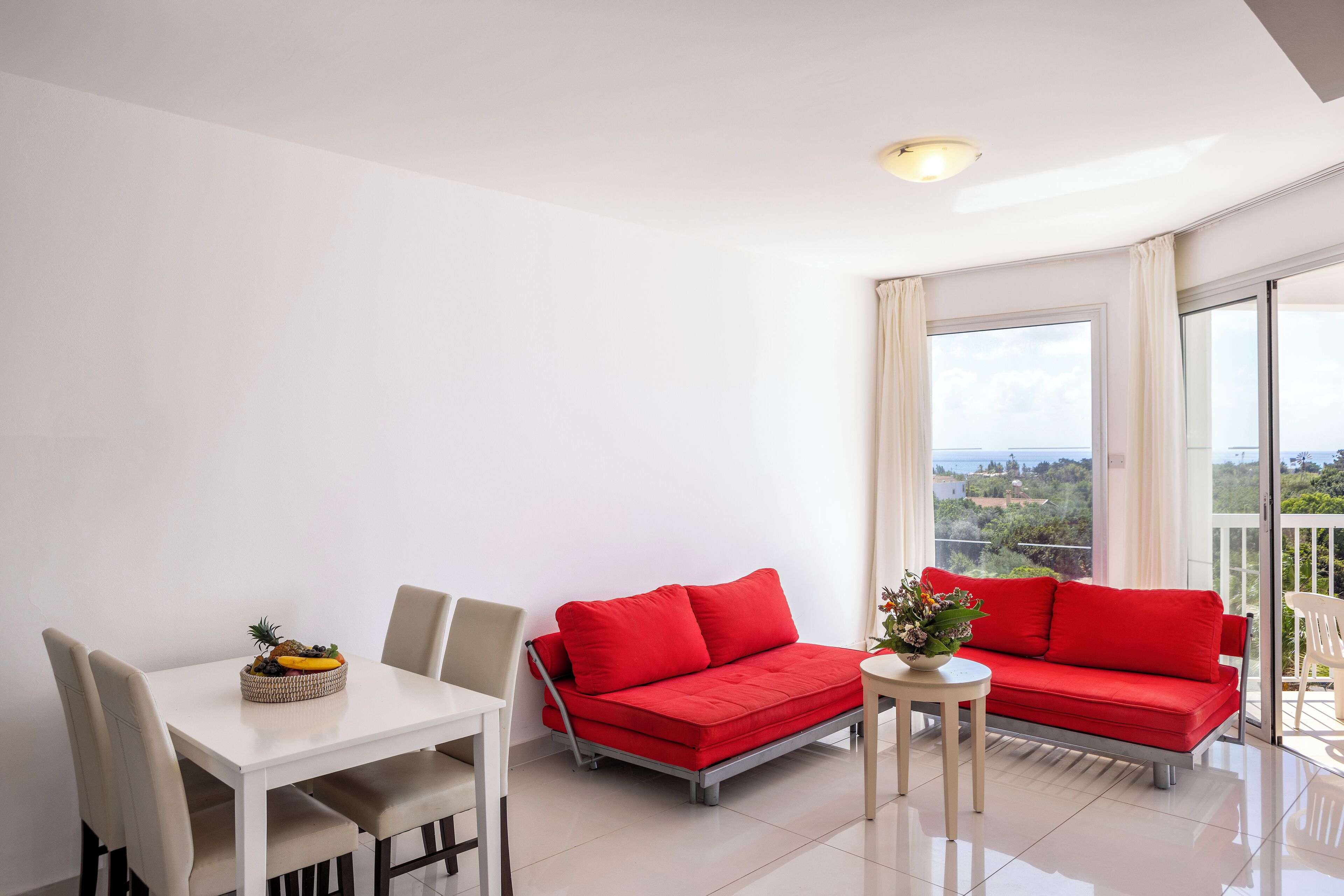 A modern living room with a white table, two red sofas, and a dining area.