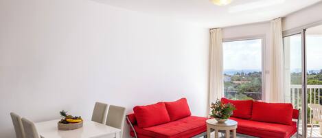 A modern living room with a white table, two red sofas, and a dining area.