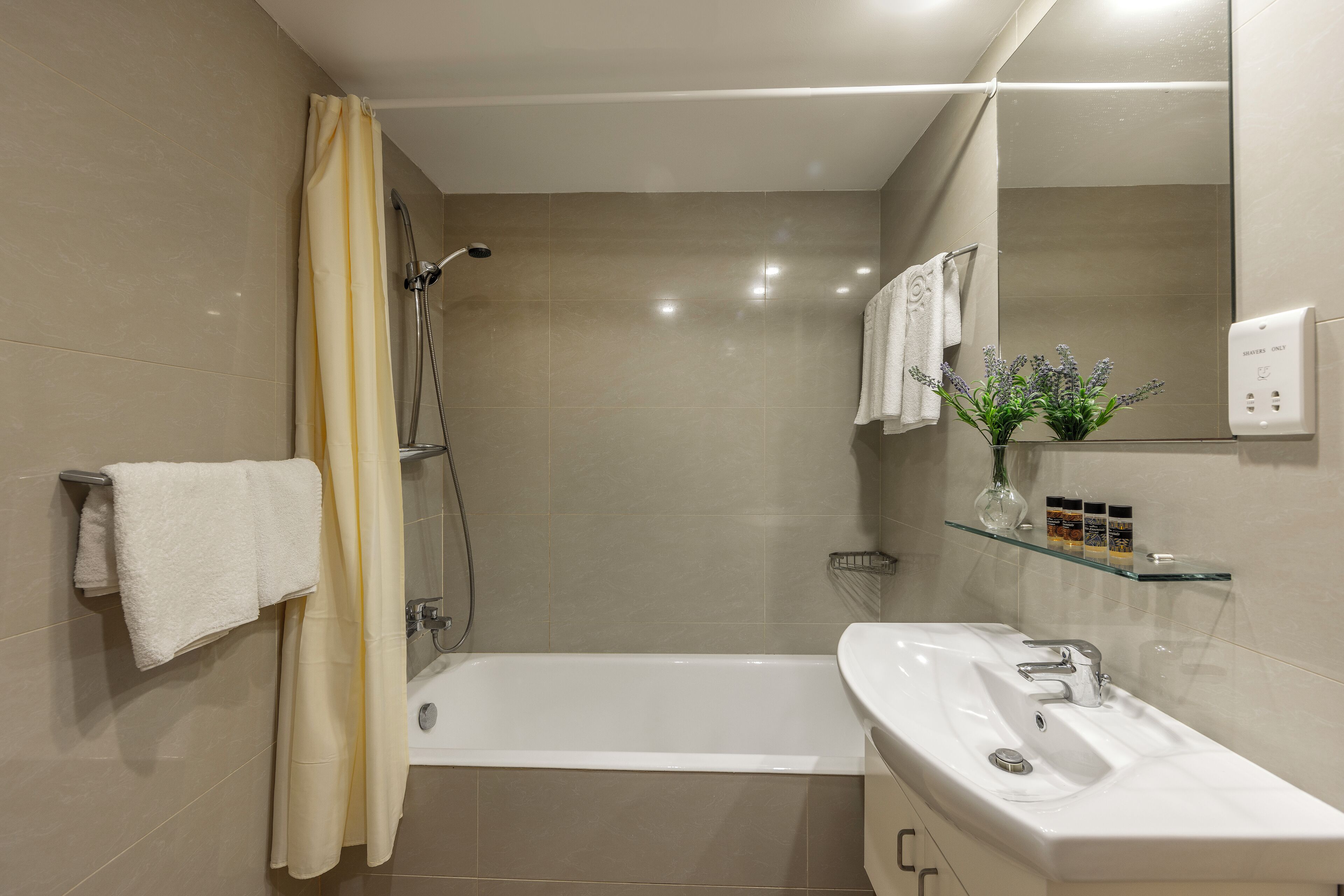 A modern bathroom with a bathtub, a shower, a glass shelf with toiletries, and a mirror.
