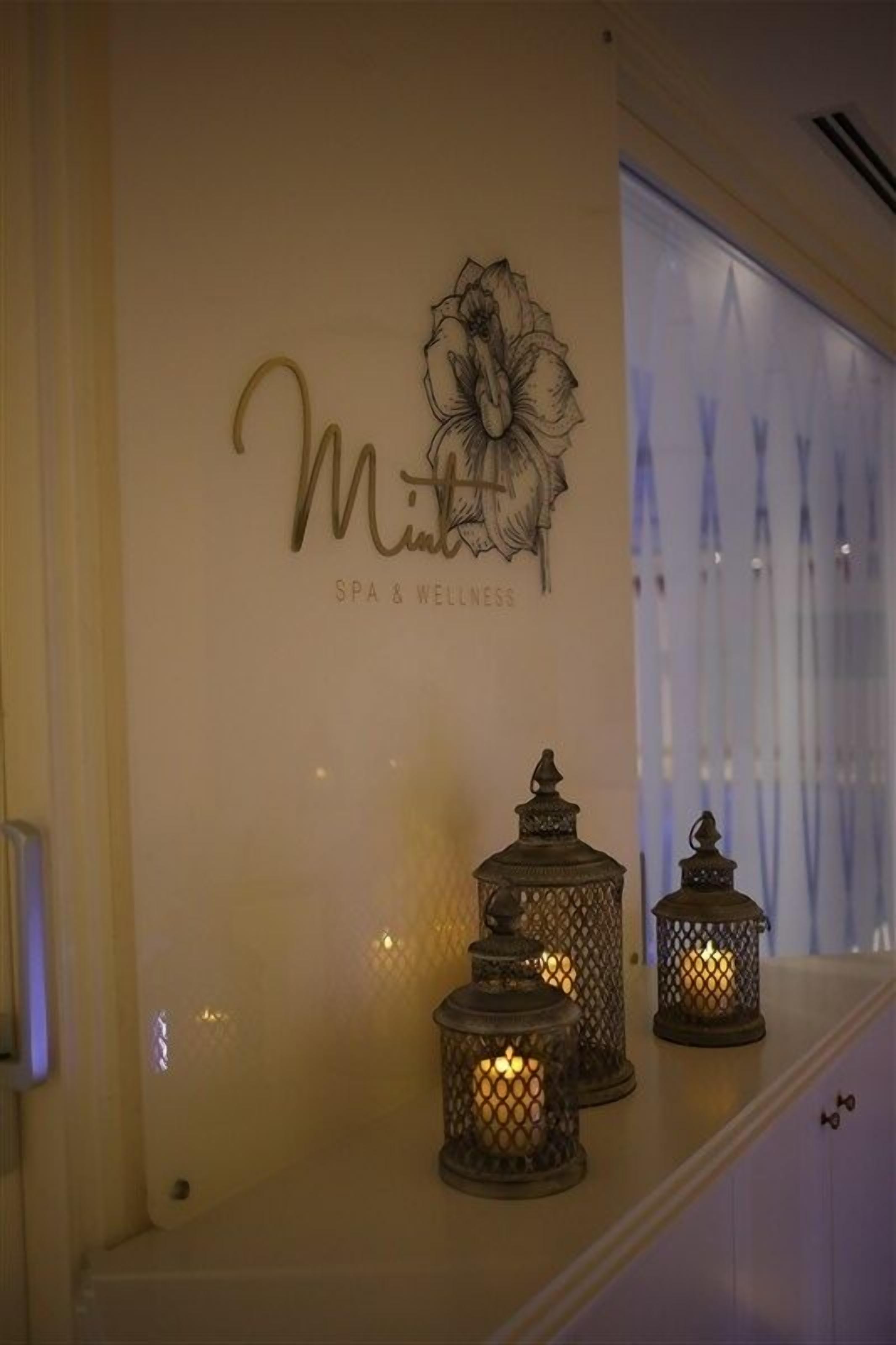 A spa and wellness sign with a floral design and three lit lanterns on a shelf.