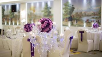 Une salle de banquet où les tables sont dressées pour un événement formel, avec des compositions florales et de la verrerie en cristal.