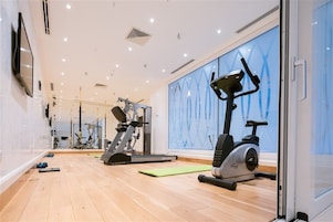 A modern gym with cardio machines, a mirrored wall, and a wooden floor.