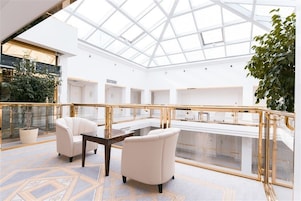 A spacious atrium with a glass ceiling, a white interior, and a golden railing.