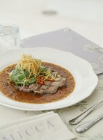 Une assiette de nourriture contenant un plat de bœuf, agrémenté de légumes verts et de lamelles de poivrons rouges, le tout servi dans une assiette blanche.
