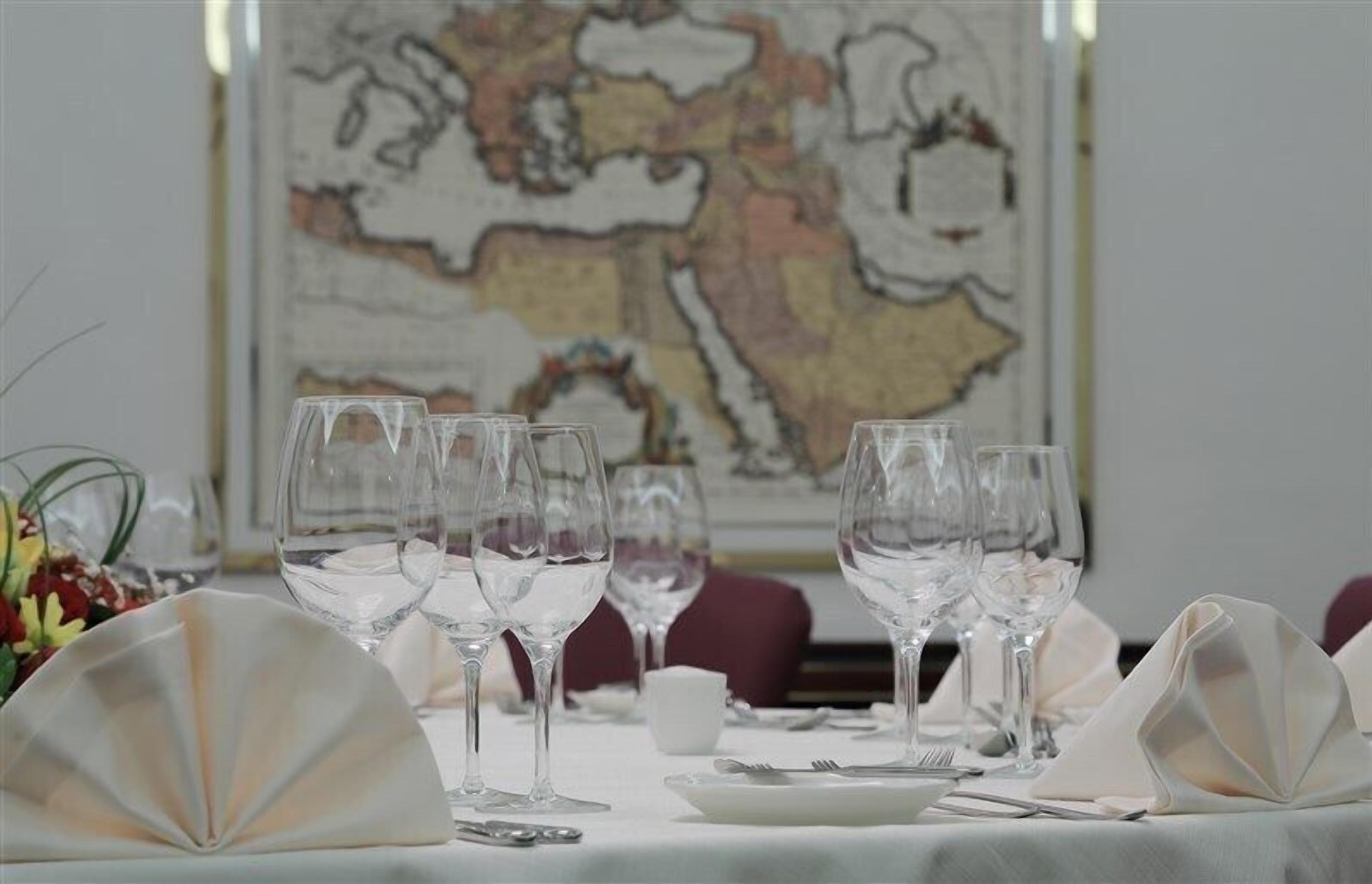 Une table à manger dressée avec de nombreux verres à vin, des assiettes et des couverts, et une carte en arrière-plan.