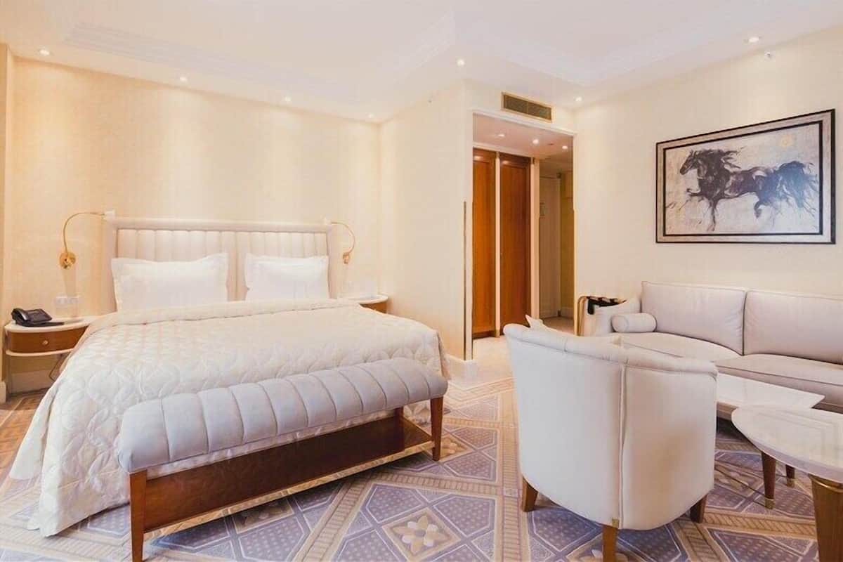A hotel room with a large bed, a sofa, a coffee table, and a painting on the wall.