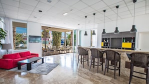 A spacious living area with a red sofa, a coffee table, and a bar area with high stools. - Hotel Napa Tsokkos (Ayia Napa)