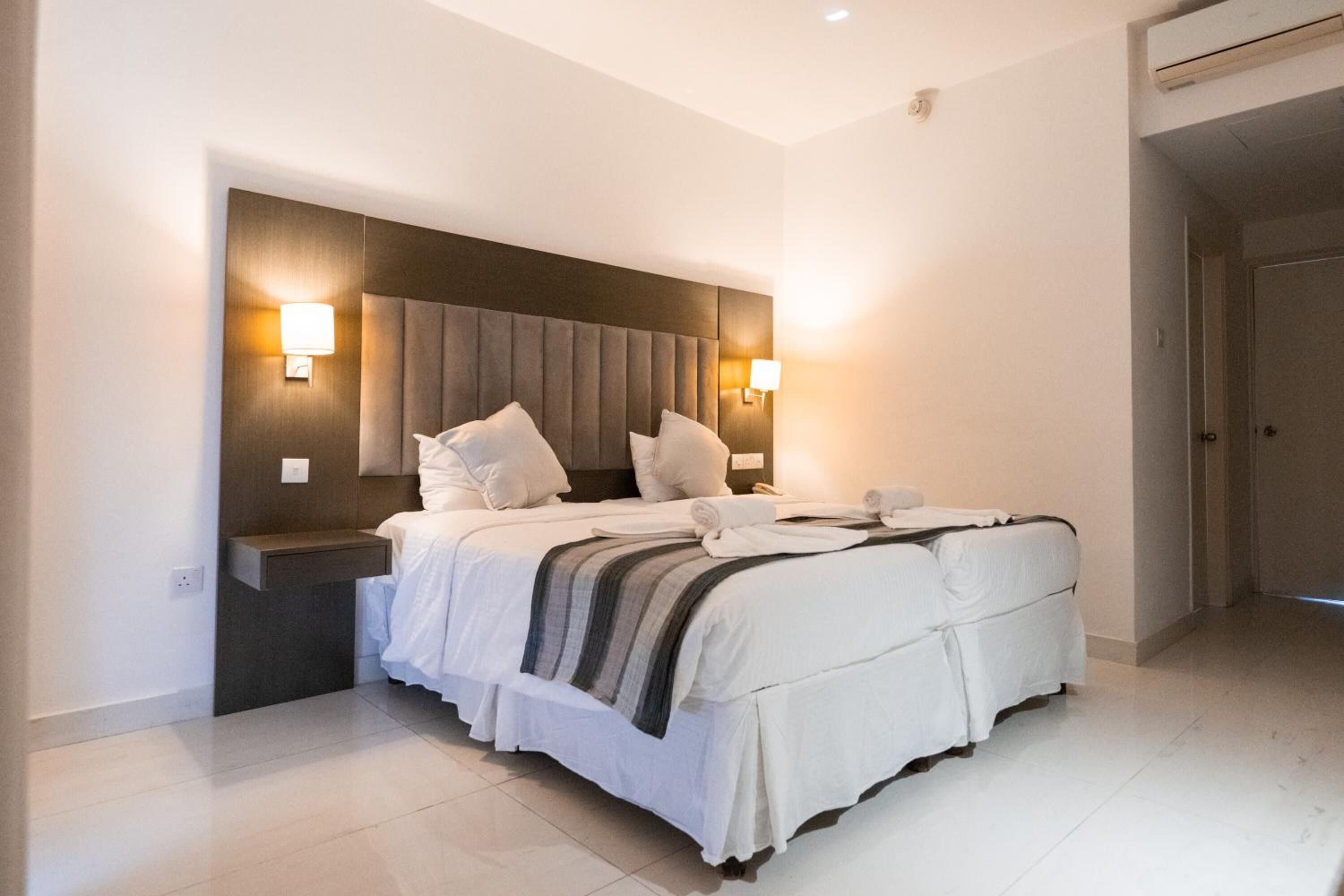 A modern hotel room with a large bed, two bedside tables, and wall-mounted lamps.