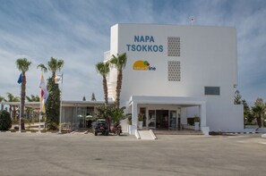 Un bâtiment moderne, orné d’une enseigne indiquant « NAPA TSOKKOS » et du logo « smartline », entouré de palmiers et de drapeaux.