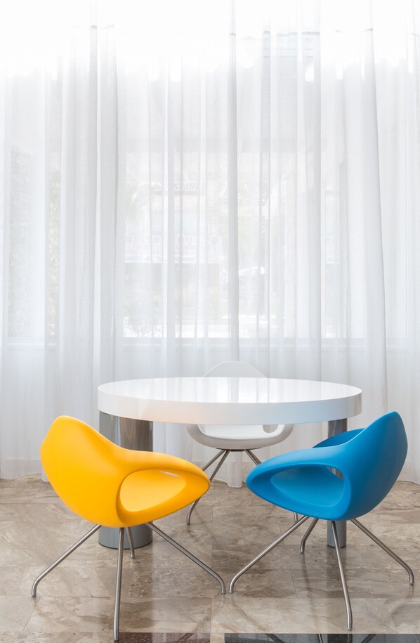 A round table with two chairs, one yellow and one blue, in front of a sheer curtain.