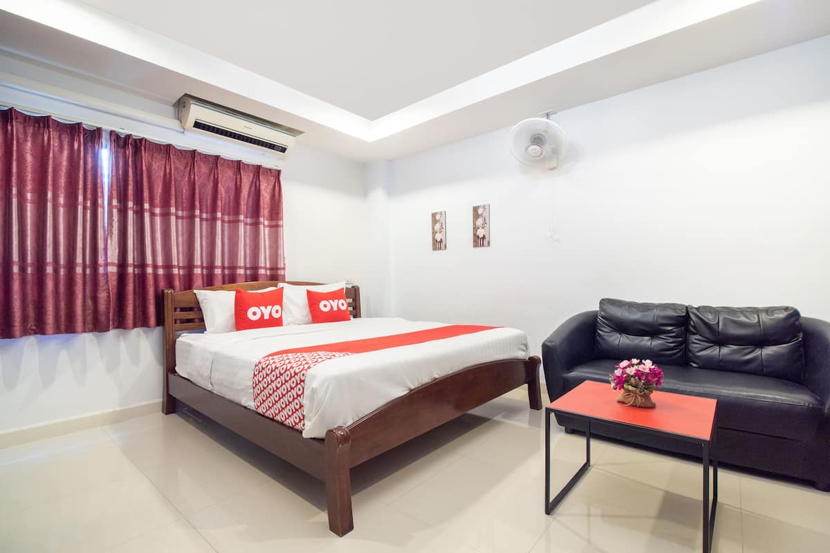 A hotel room with a bed, a black leather sofa, a small table with a vase of flowers, and a red and white bedspread.