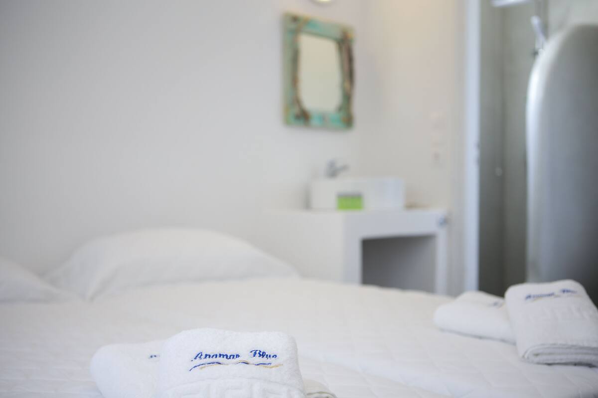 A hotel room with a neatly made bed, a small bedside table with a lamp, and a wall-mounted mirror.