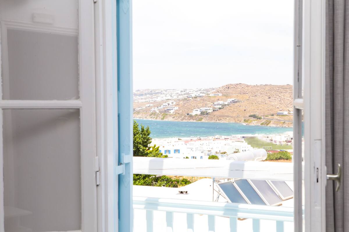 A view from a balcony with a coastal landscape, including buildings and a hill.