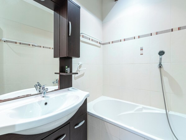 A bathroom with a white sink, dark wooden cabinet, and a white bathtub with a shower head.